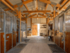 Interior of a horse barn showing stalls, wide aisle, and organized tack room