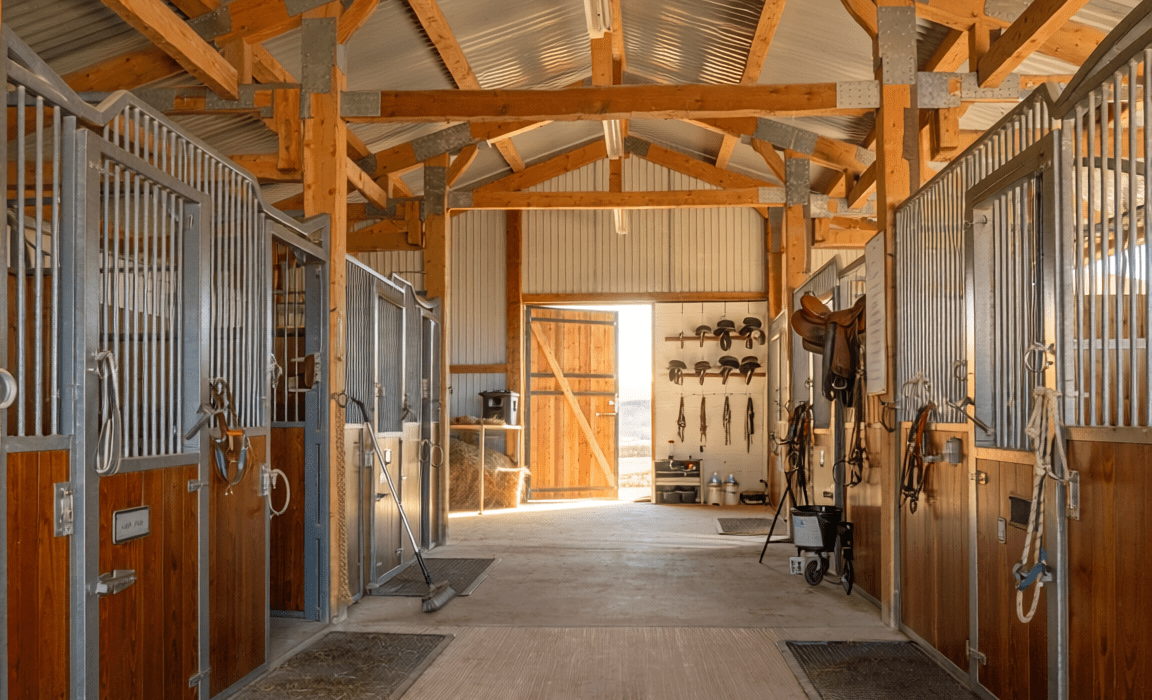 Interior of a horse barn showing stalls, wide aisle, and organized tack room